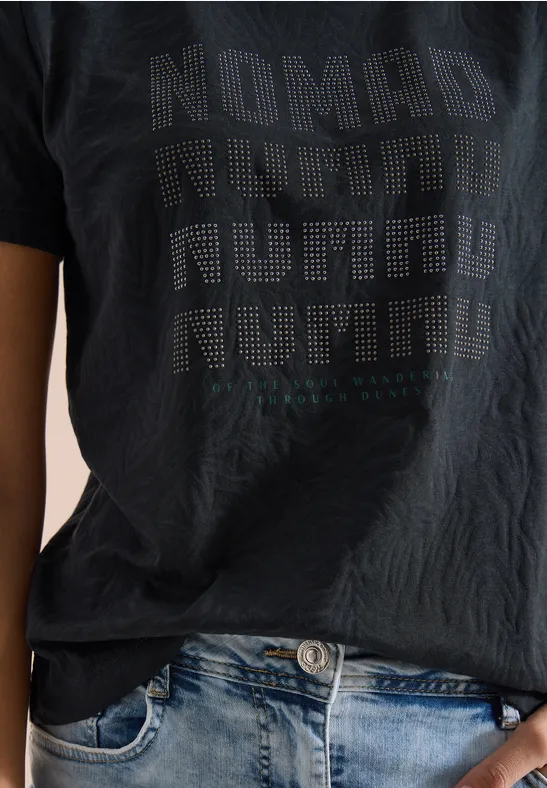 Oberkörper in Jeans und schwarzem T-Shirt mit aufgedrucktem 'Nomad'-Motiv.