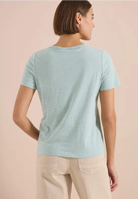 Rückansicht einer Frau in hellblauem T-Shirt und beigen Hosen vor beigem Hintergrund.
