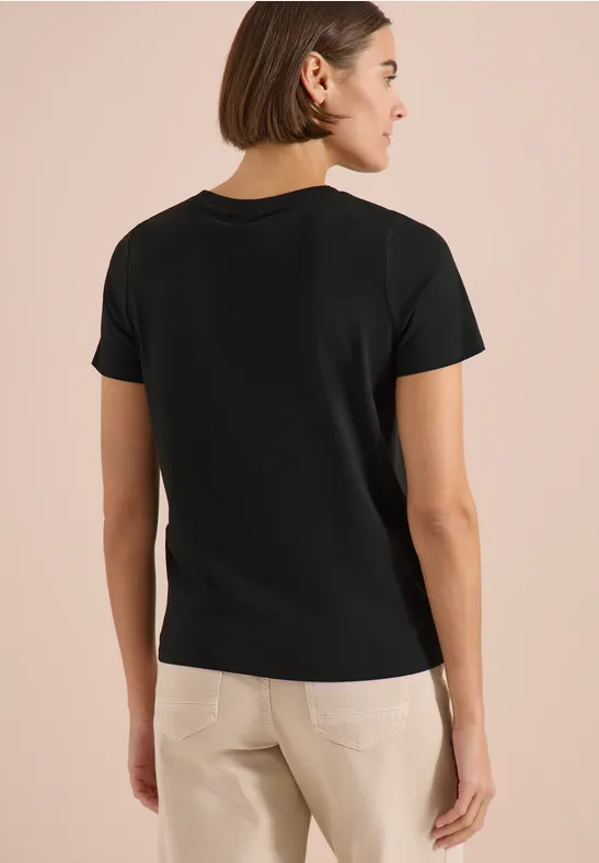 Frau in schwarzem T-Shirt und beigen Hosen, von hinten fotografiert.