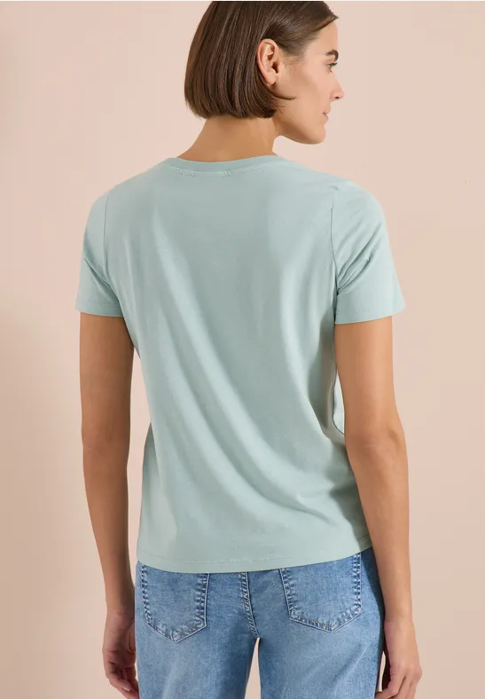 Frau von hinten in hellblauem T-Shirt und Jeans, schulterlanges braunes Haar.