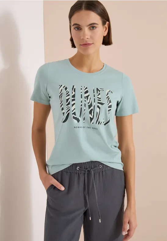Frau trägt hellblaues T-Shirt mit Zebra-Print-Schriftzug und dunkelgraue, locker sitzende Jogginghose.