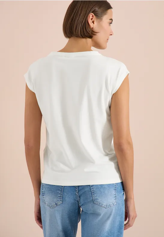 Achteraanzicht van een vrouw in een wit T-shirt en blauwe spijkerbroek voor een effen achtergrond.