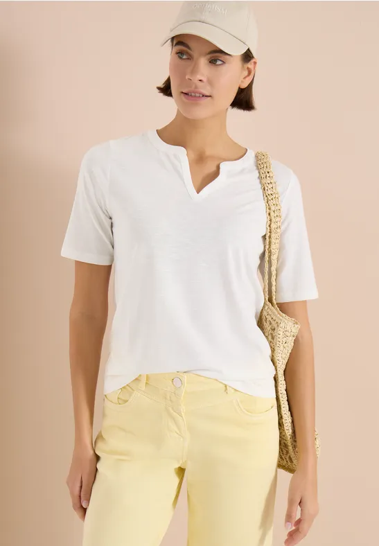 Person trägt weißes T-Shirt, gelbe Hose, weiße Schirmmütze und geflochtene Umhängetasche.