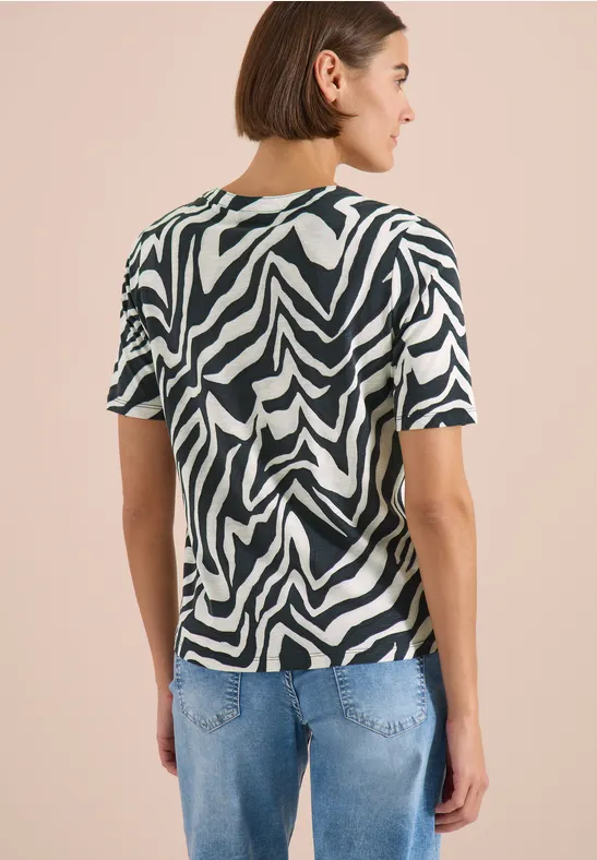 Achteraanzicht van een persoon met kort haar in een zebraprint-t-shirt en blauwe jeans.