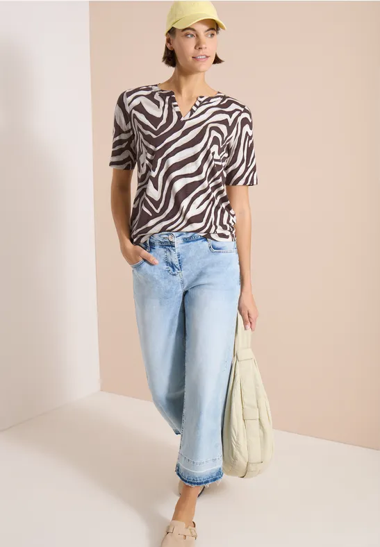 Persoon draagt zebra T-shirt, lichte jeans en houdt een beige tas vast.