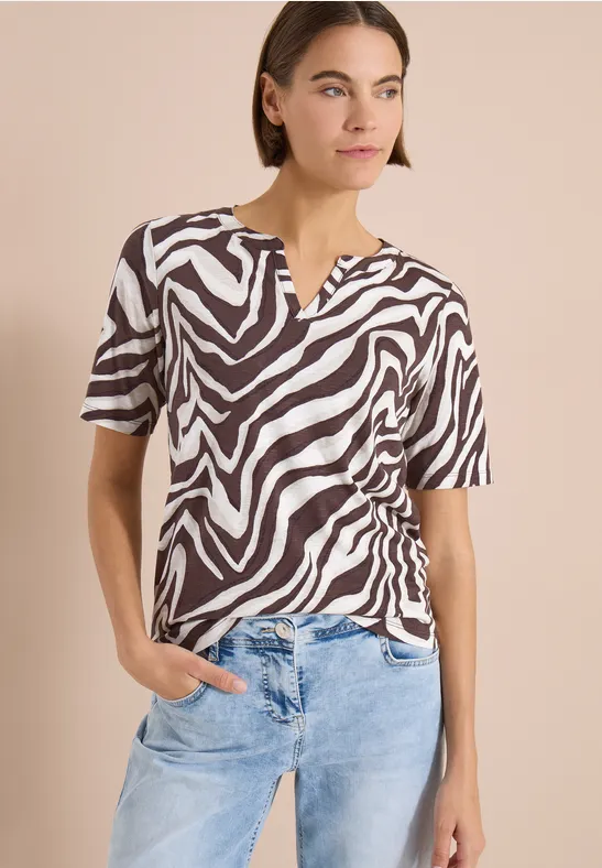 Vrouw draagt zwart-wit zebraprint top met korte mouwen en V-hals, gecombineerd met een lichtblauwe jeans.