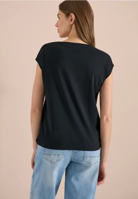 Femme de dos portant un t-shirt noir et un jean bleu clair sur fond neutre.