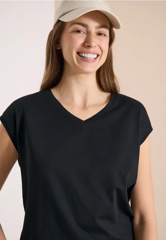 Femme portant un t-shirt noir à col en V et une casquette beige clair sur fond neutre.