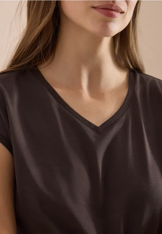 Vrouw met donkerbruin V-hals shirt, alleen bovenlijf en deel van gezicht zichtbaar.