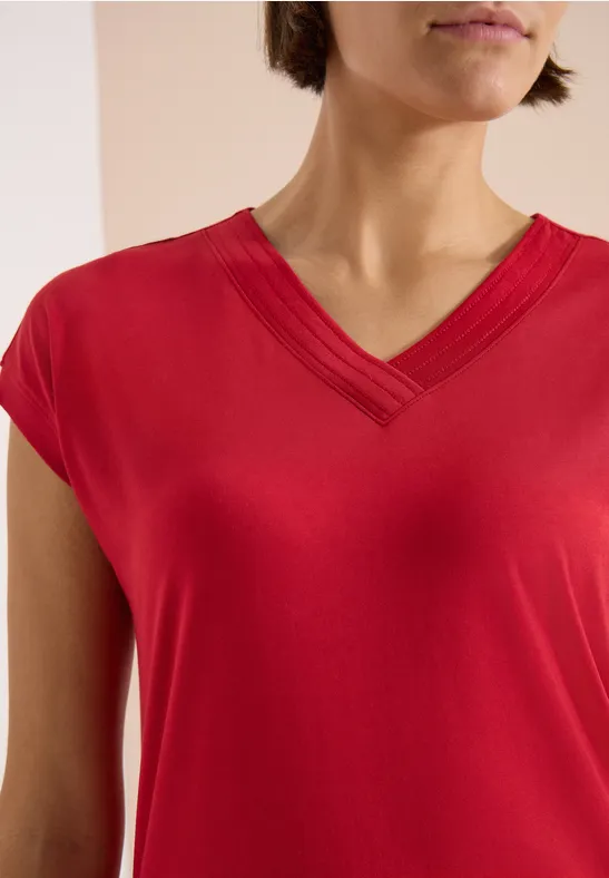 Rotes V-Ausschnitt-T-Shirt an einer Person, enger Bildausschnitt von Schulter bis Brust.