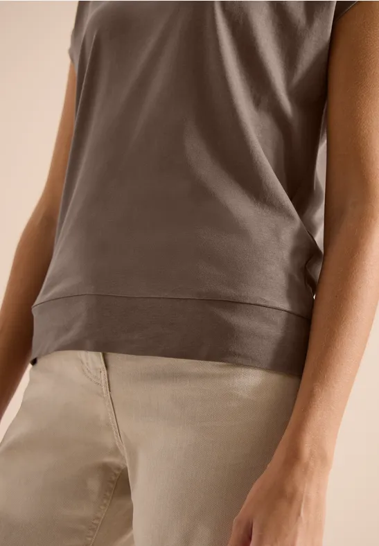 Eine Nahaufnahme eines Oberkörpers in braunem Top und beige Hose, mit Blick auf Taille und Arme.