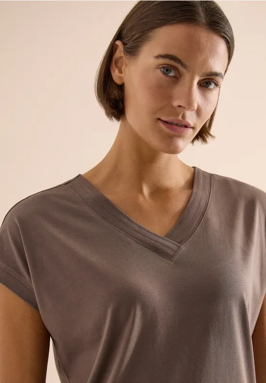 Person trägt taupefarbenes, kurzärmeliges V-Ausschnitt-Shirt.