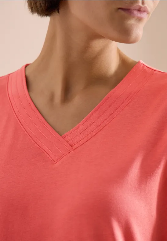 Nahaufnahme eines korallfarbenen T-Shirts mit V-Ausschnitt.