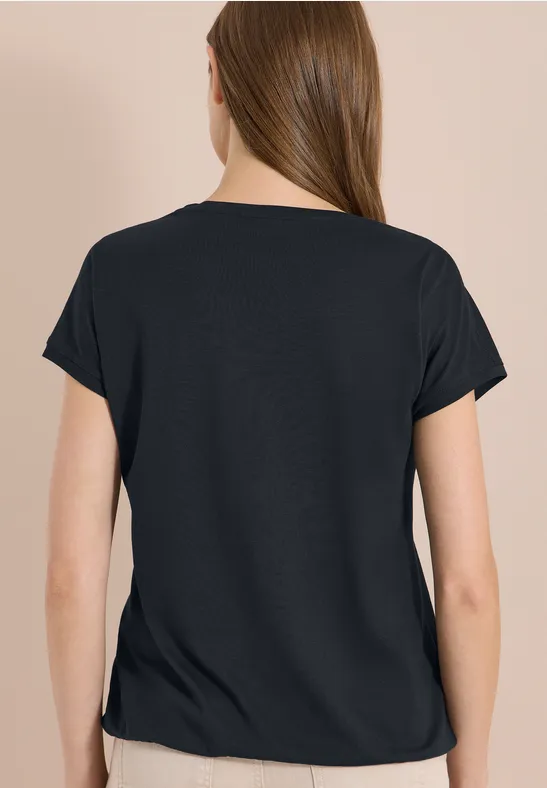 Rückansicht einer Person mit schwarzem T-Shirt vor hellem Hintergrund.