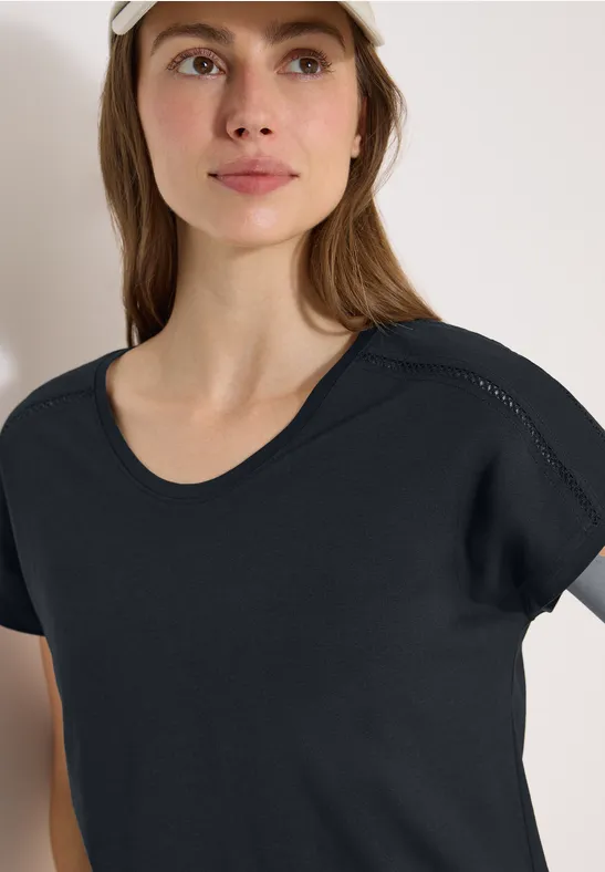 Frau trägt schlichtes schwarzes T-Shirt, Gesicht unscharf.