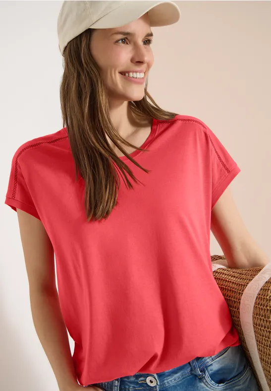 Frau in rotem T-Shirt und Jeans, mit heller Kappe und Strohtasche