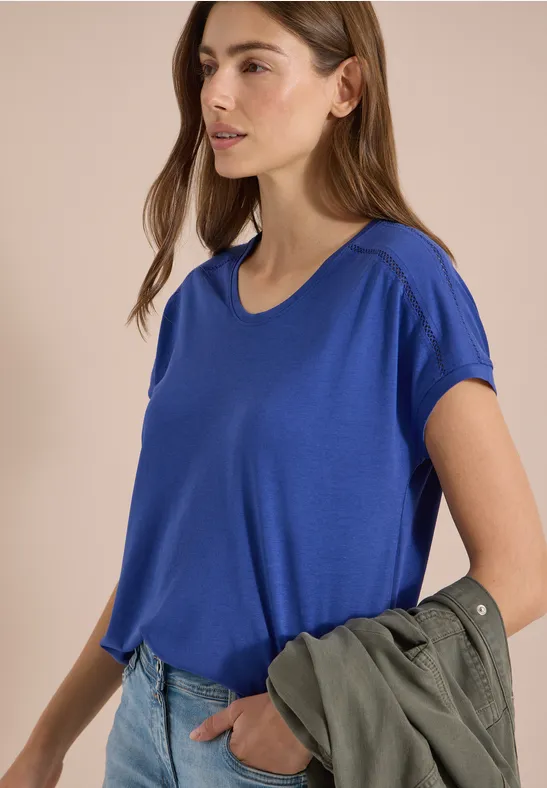 Vrouw met wazig gezicht in blauw t-shirt, houdt groene jas in haar hand.