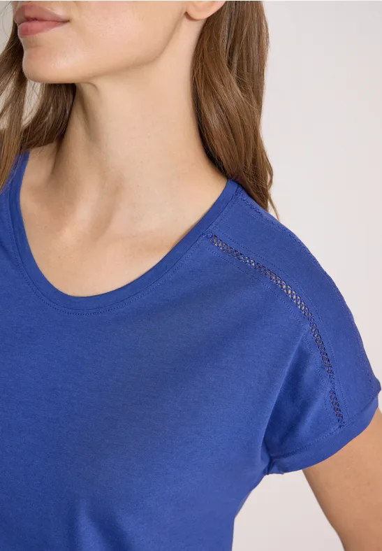 Close-up van een vrouw in een blauw t-shirt, bovenlichaam tot de kin zichtbaar.