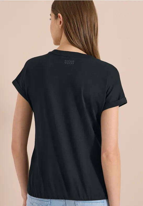 Frau von hinten in schlichtem schwarzen T-Shirt vor beigem Hintergrund
