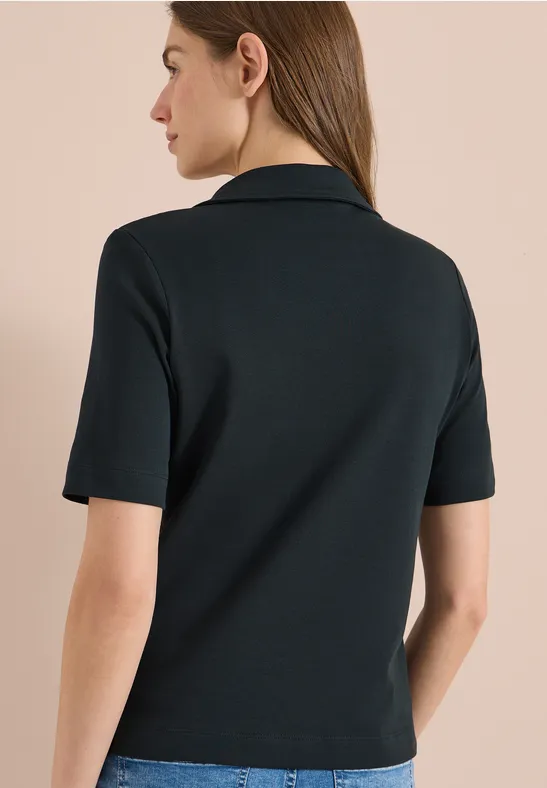 Eine Person von hinten in schwarzem, kurzärmeligem Oberteil vor hellem Hintergrund.