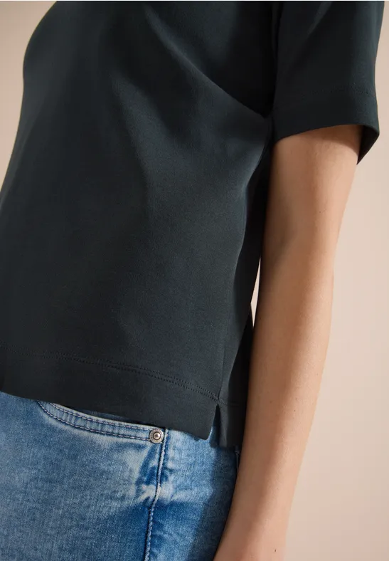 Seitenansicht eines Oberkörpers in dunkelgrünem T-Shirt mit kurzen Ärmeln und blauer Jeans.