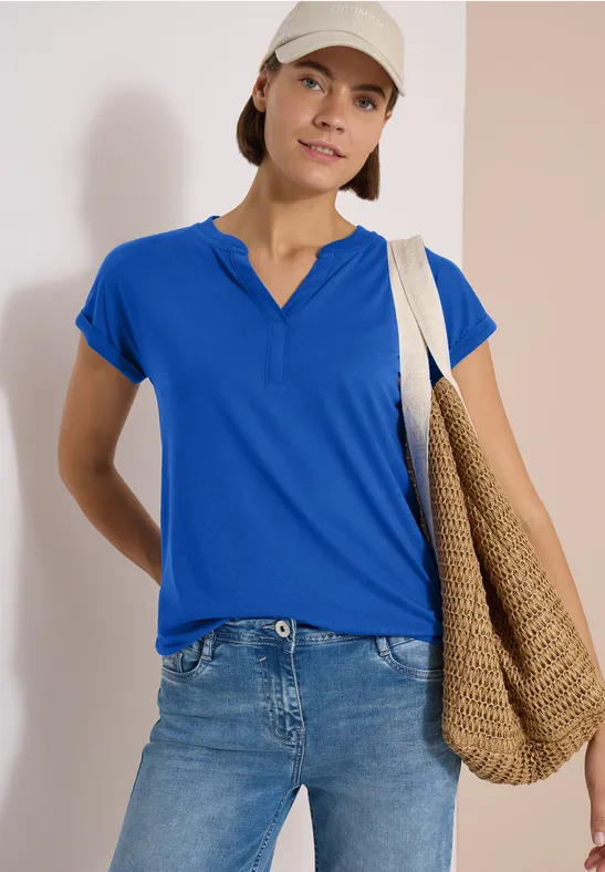 Person in blauem T-Shirt und Jeans trägt große Strohtasche über der Schulter.