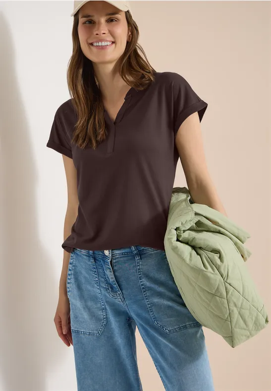 Frau in dunklem T-Shirt und Jeans, hält eine hellgrüne gesteppte Jacke.