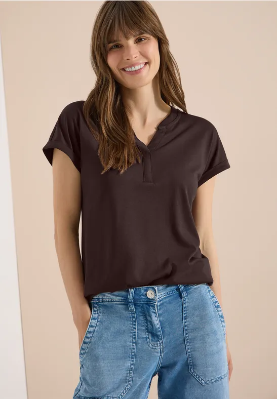 Frau in schwarzem Poloshirt und blauen Jeans vor hellem Hintergrund.
