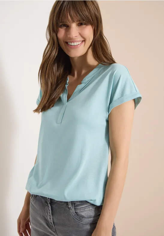 Frau trägt hellblaues kurzärmeliges Polo-Shirt und Jeans, Gesicht unkenntlich.