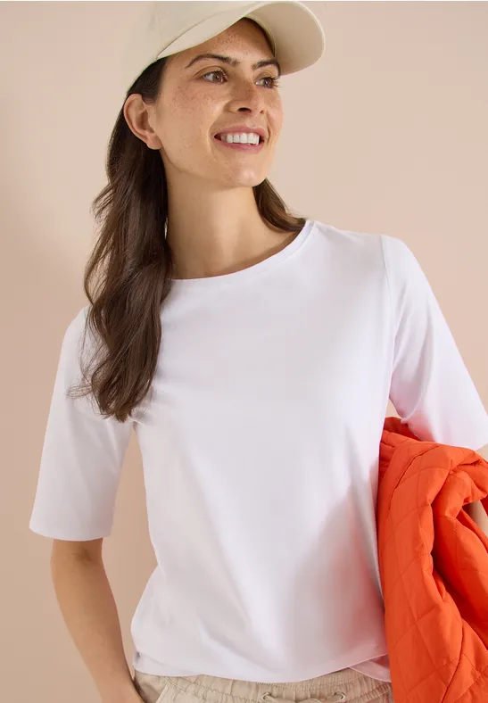 Vrouw in wit T-shirt en pet houdt een oranje jas vast, portret met geblurd gezicht.