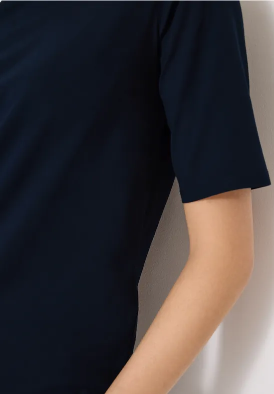 Zijdelingse weergave van een arm in een marineblauw T-shirt met korte mouwen voor een witte muur.