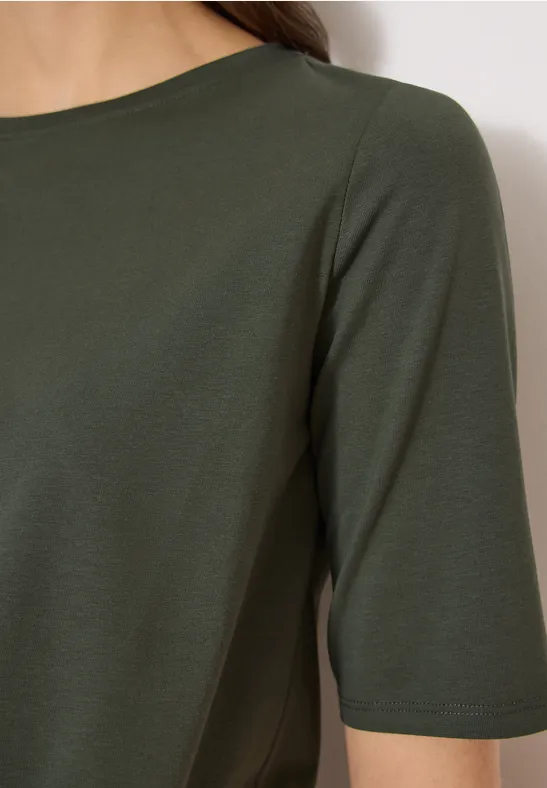 Close-up van een persoon in een olijfgroen shirt met driekwart mouwen.