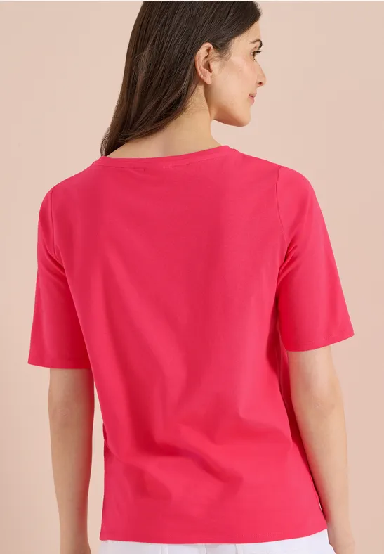 Rugaanzicht van een vrouw met lang bruin haar in een roze T-shirt tegen een lichte achtergrond.
