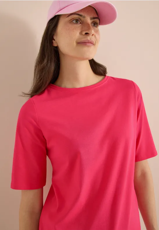Een persoon draagt een roze t-shirt en een bijpassende pet tegen een lichte achtergrond.