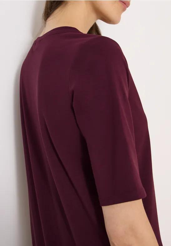 Gedeeltelijke weergave van een vrouw in een bordeauxrode top met driekwartmouwen.