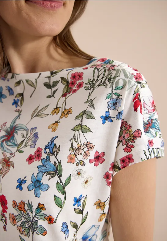 Een wit shirt met een kleurrijk bloemenpatroon en korte mouwen.
