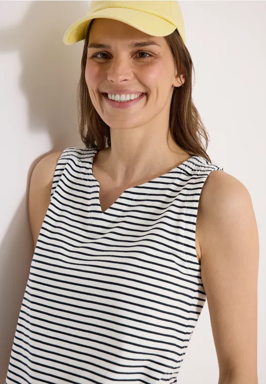 Eine Person in gestreiftem Top und gelbem Hut vor heller Wand.