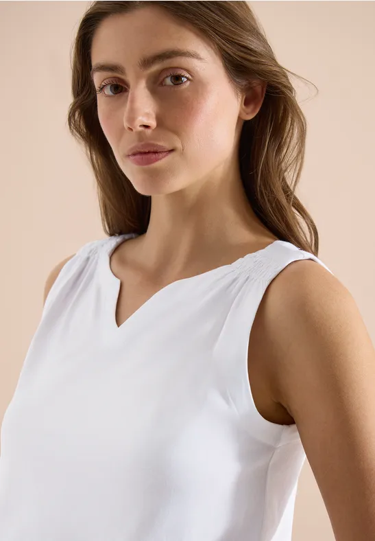 Frau in weißem, ärmellosem Top mit V-Ausschnitt, die entspannt posiert.