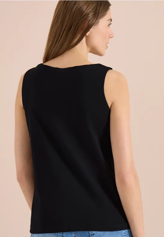 Rückansicht einer Frau in schwarzem ärmellosen Oberteil vor hellem Hintergrund.