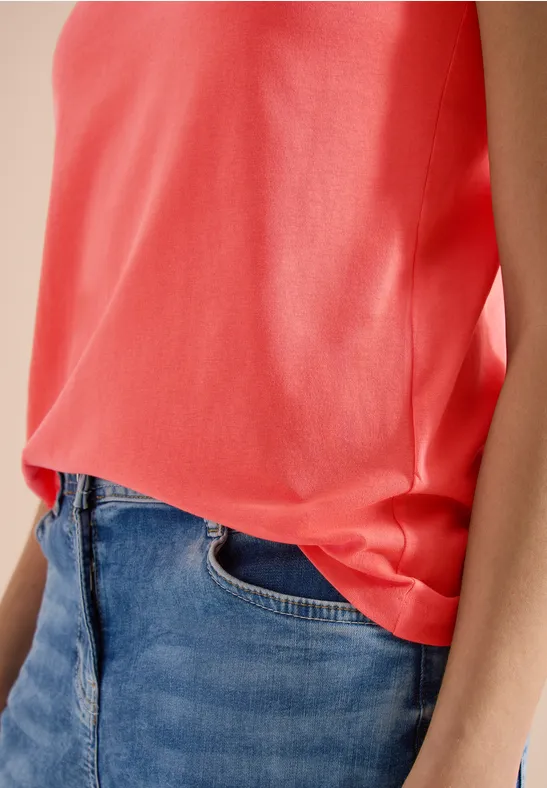 Iemand draagt een mouwloos koraalkleurig topje, ingestopt in een klassieke blauwe spijkerbroek.