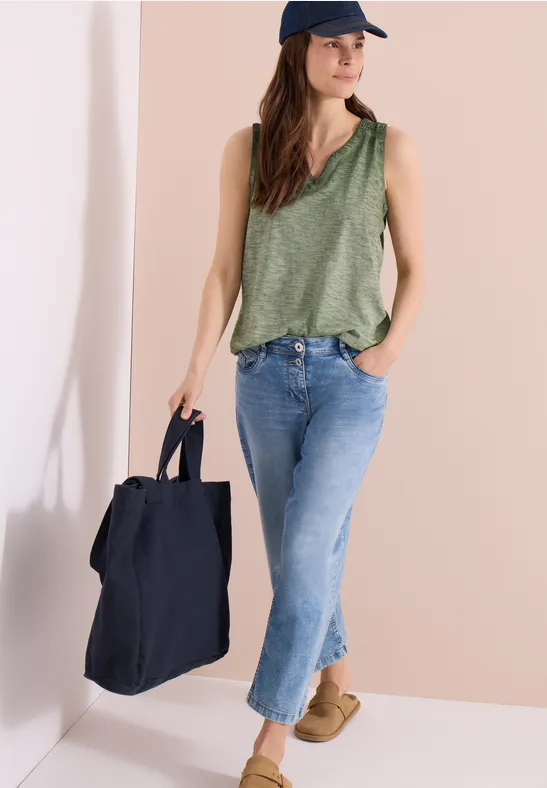 Vrouw in groen hemdje, spijkerbroek en pet met grote zwarte tas en beige schoenen.