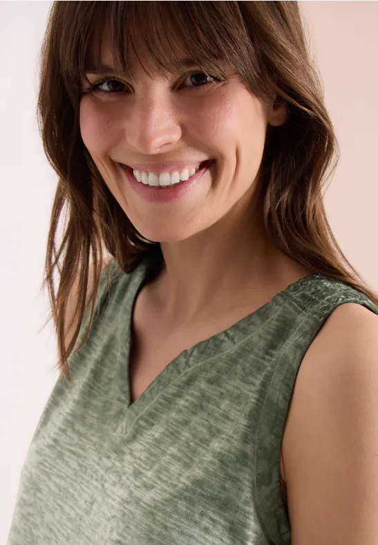 Persoon draagt groene mouwloze V-hals top, gezicht vaag, halflang haar.