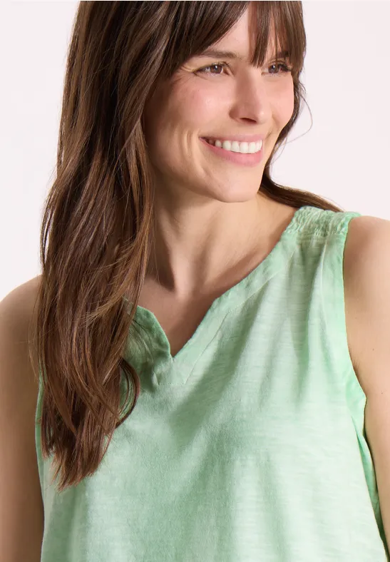 Vrouw draagt mouwloos lichtgroen linnen topje, ronde hals en losse pasvorm.