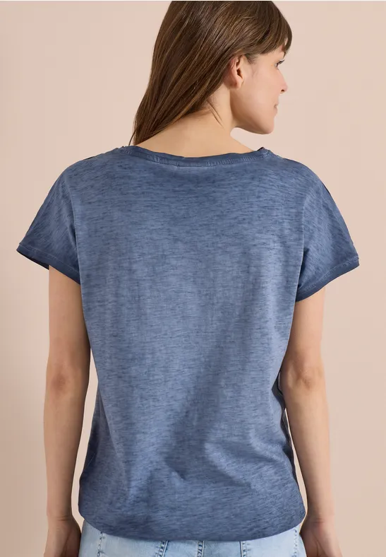 Rückansicht einer Frau mit kurzem blauen T-Shirt und abgerundetem Saum vor beigem Hintergrund.