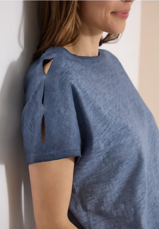 Nahaufnahme einer Frau in einem blauen, kurzärmligen Pullover mit Schlitz am Ärmel und rundem Ausschnitt.