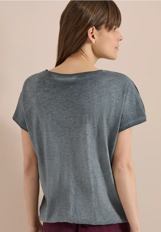 Achteraanzicht van een vrouw in losvallend grijs t-shirt voor een beige achtergrond.