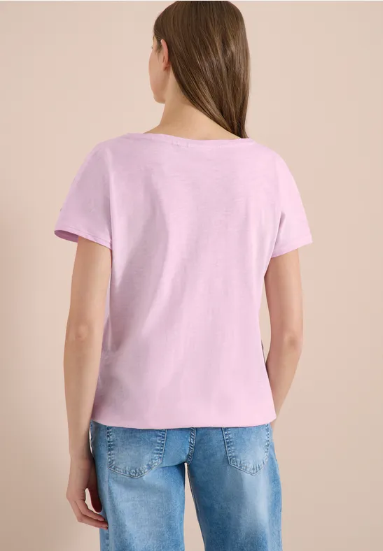 Frau von hinten in hellem rosa T-Shirt und blauen Jeans vor neutralem Hintergrund.