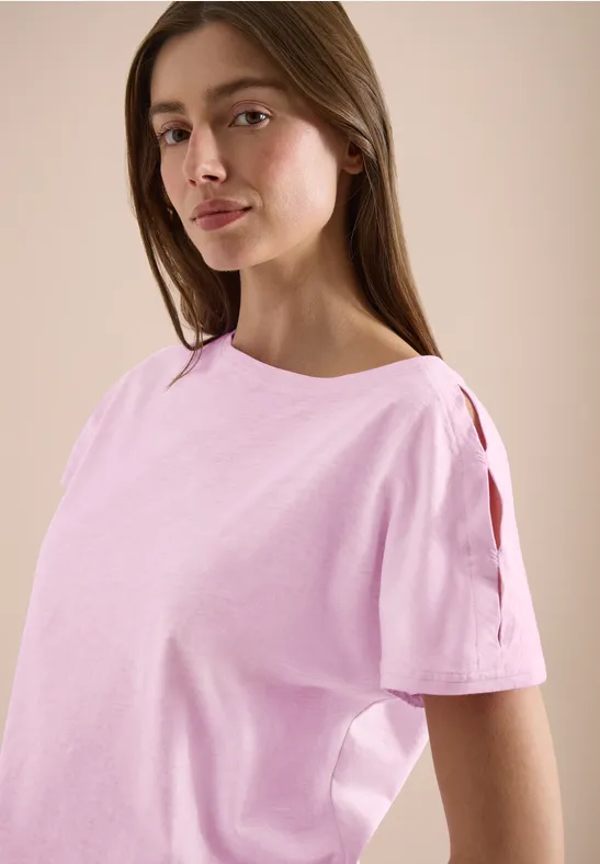 Frauen-Oberteil in zartem Rosa mit Cut-Out-Ärmeln vor neutralem Hintergrund.