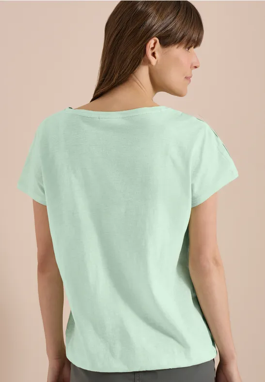 Rückenansicht einer Frau im mintgrünen T-Shirt vor einfarbigem Hintergrund.