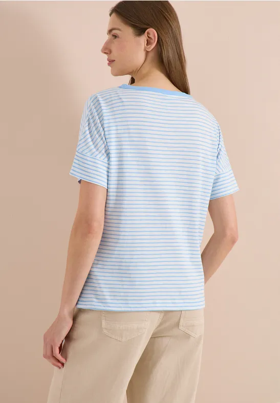 Eine Frau von hinten trägt ein hellblau-weiß gestreiftes T-Shirt mit kurzen Ärmeln und eine helle beige Hose.